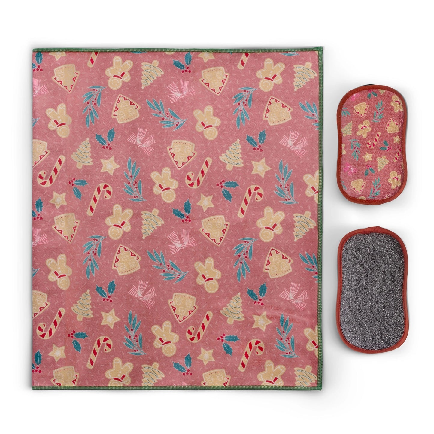 A rectangular holiday-themed cleaning cloth with a festive pattern of gingerbread cookies, candy canes, stars, and holly leaves on a dusty pink background, shown alongside two oval scrubber pads on a white background.