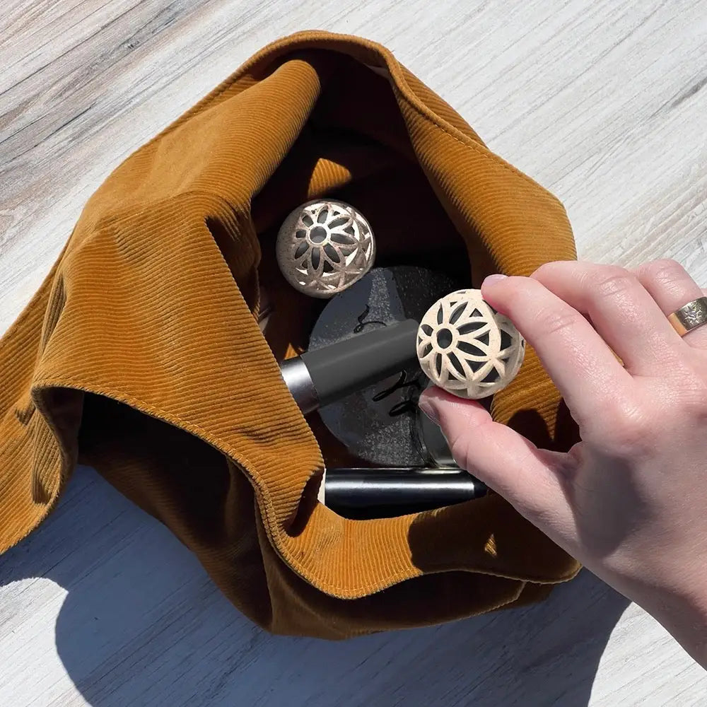 A hand holds a cream-colored, intricately carved spherical object with a floral pattern.