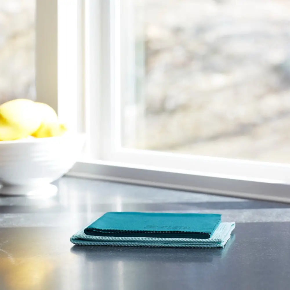 Teal microfiber cleaning cloth with a textured edge, neatly folded on a dark countertop.