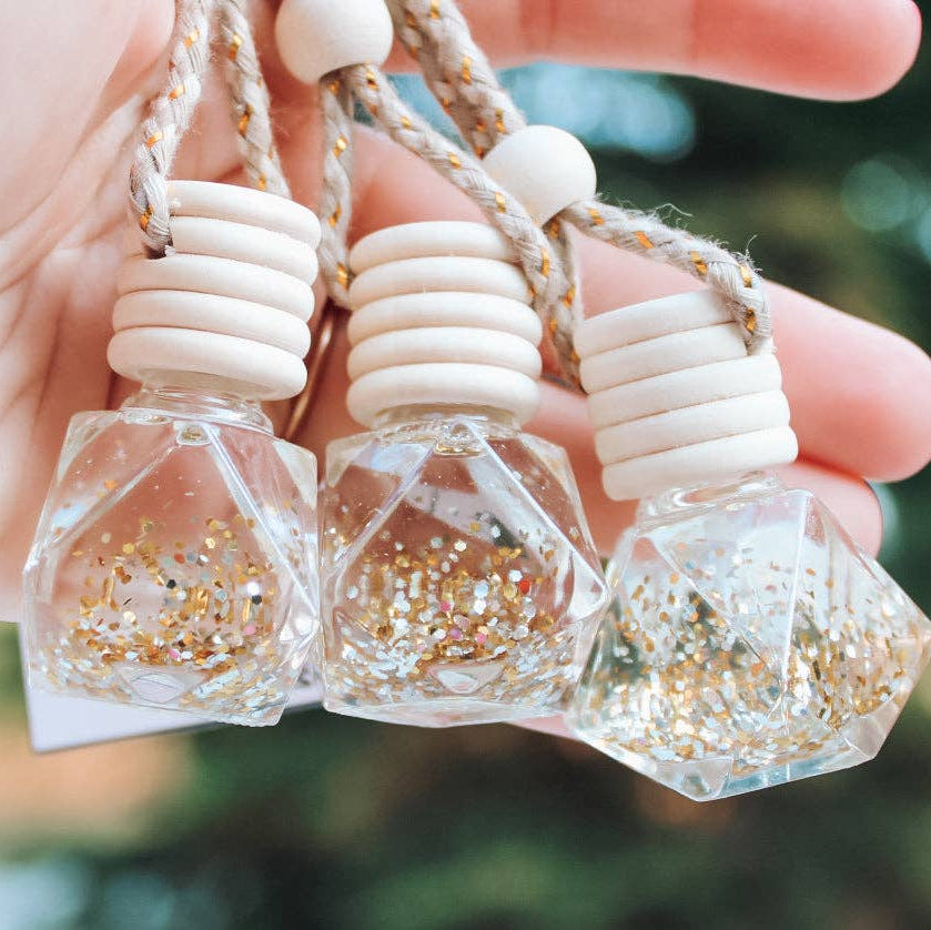Three small hexagonal bottles with glittery contents held by a hand against a blurred natural background.