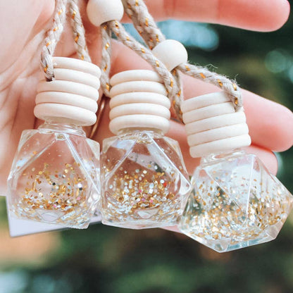 Three small hexagonal bottles with glittery contents held by a hand against a blurred natural background.
