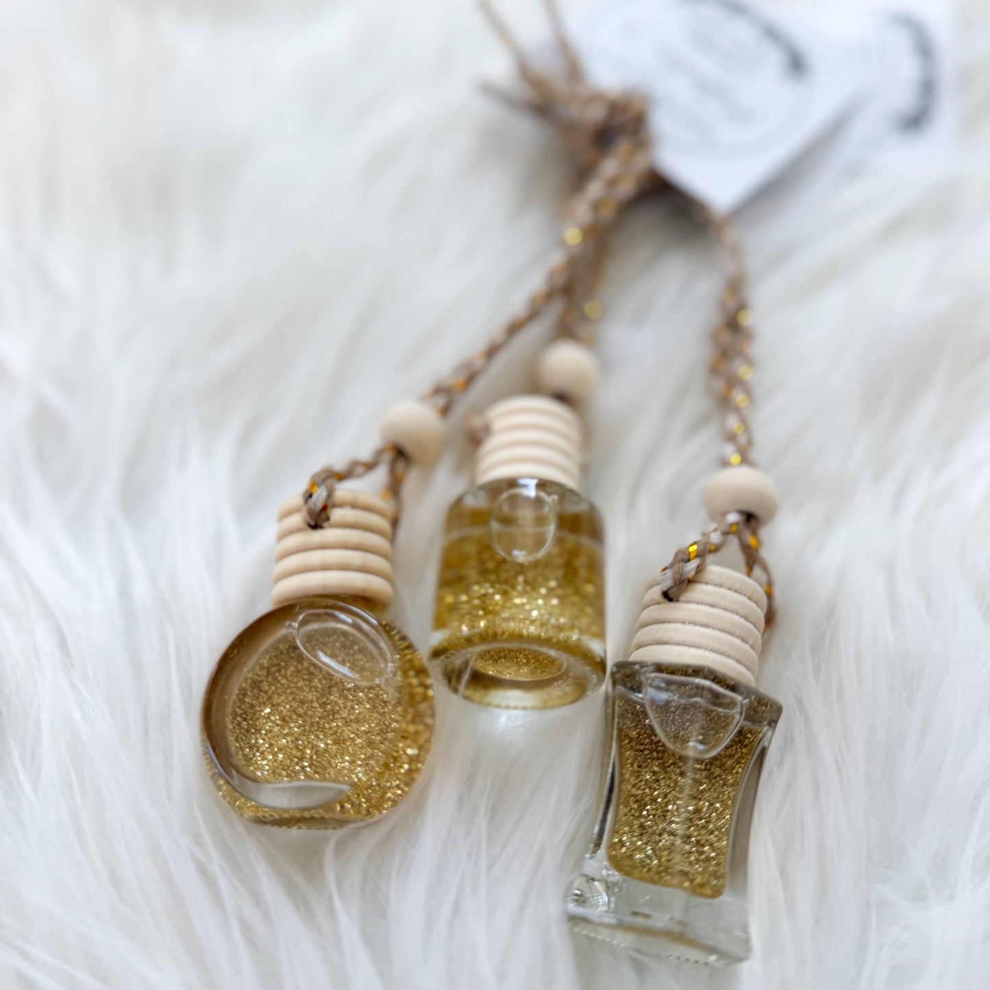 Three small glass bottles with gold glitter contents on a white fluffy surface
