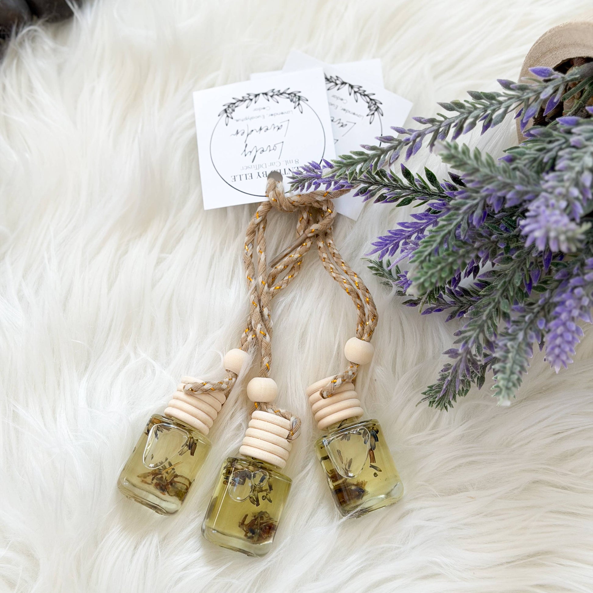 Three small glass bottles with natural elements on a fluffy white surface with lavender flowers.