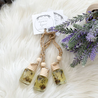Three small glass bottles with natural elements on a fluffy white surface with lavender flowers.