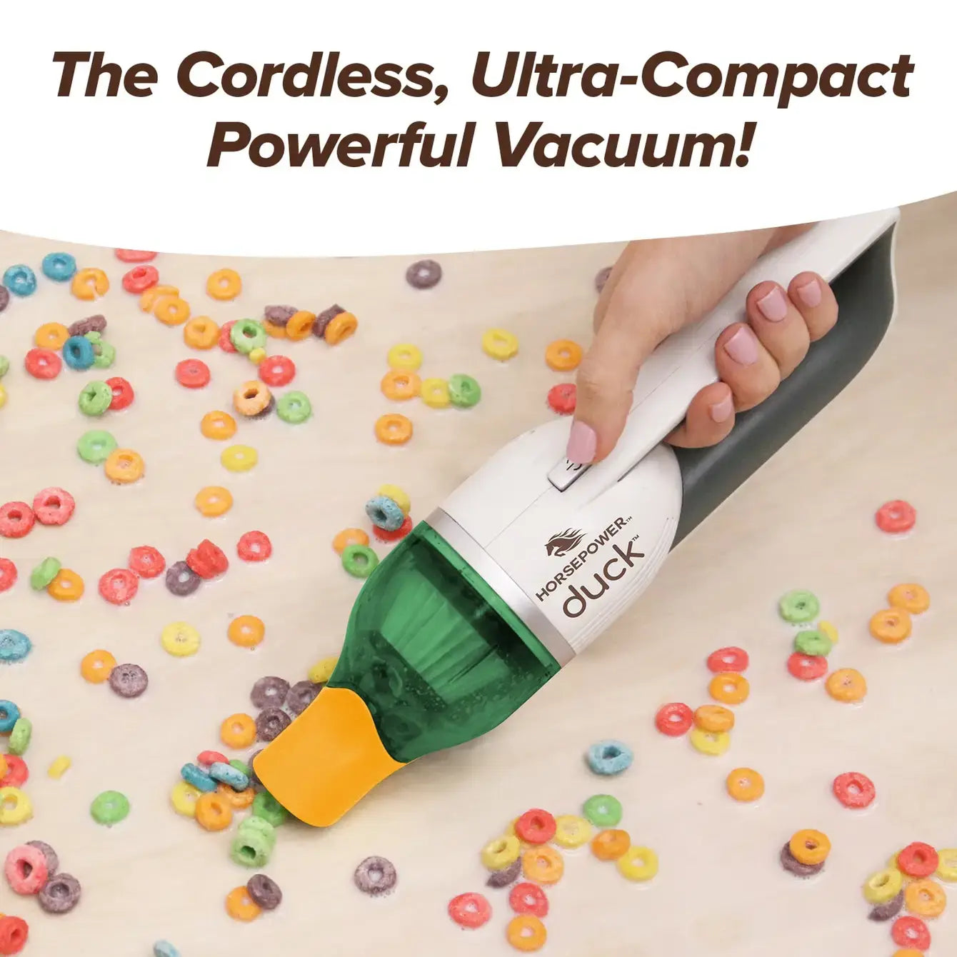 Hand using a cordless vacuum cleaner on a surface with colorful cereal loops.