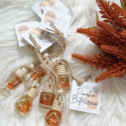A set of small glass bottles with wooden dropper caps and twisted cords, filled with amber-orange liquid and glitter, arranged on a white faux-fur surface with dried orange foliage and printed tags.