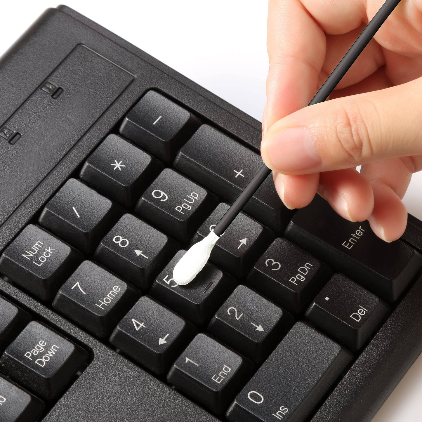 Person cleaning a black keyboard with a Q-tip on a white background