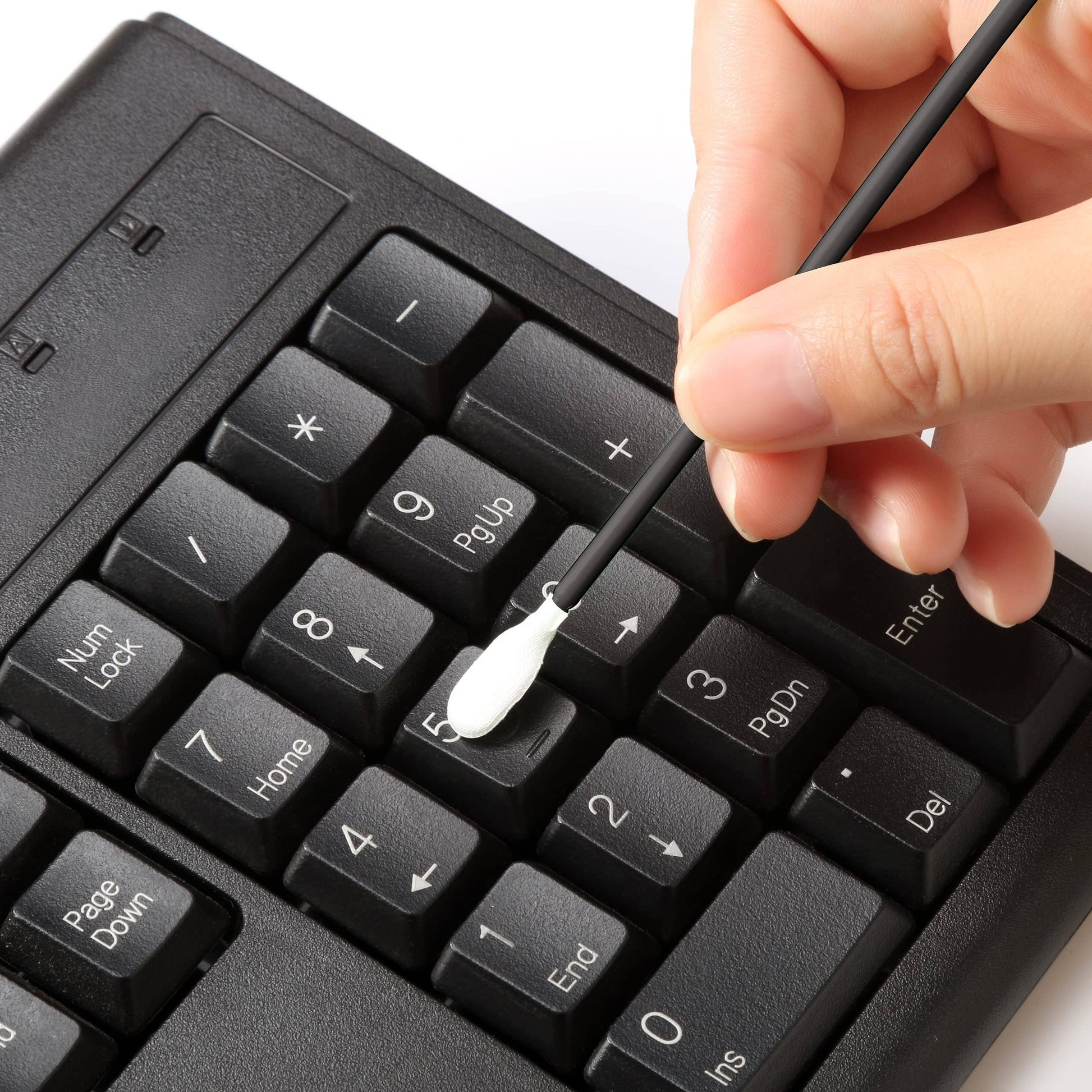Person cleaning a black keyboard with a Q-tip on a white background
