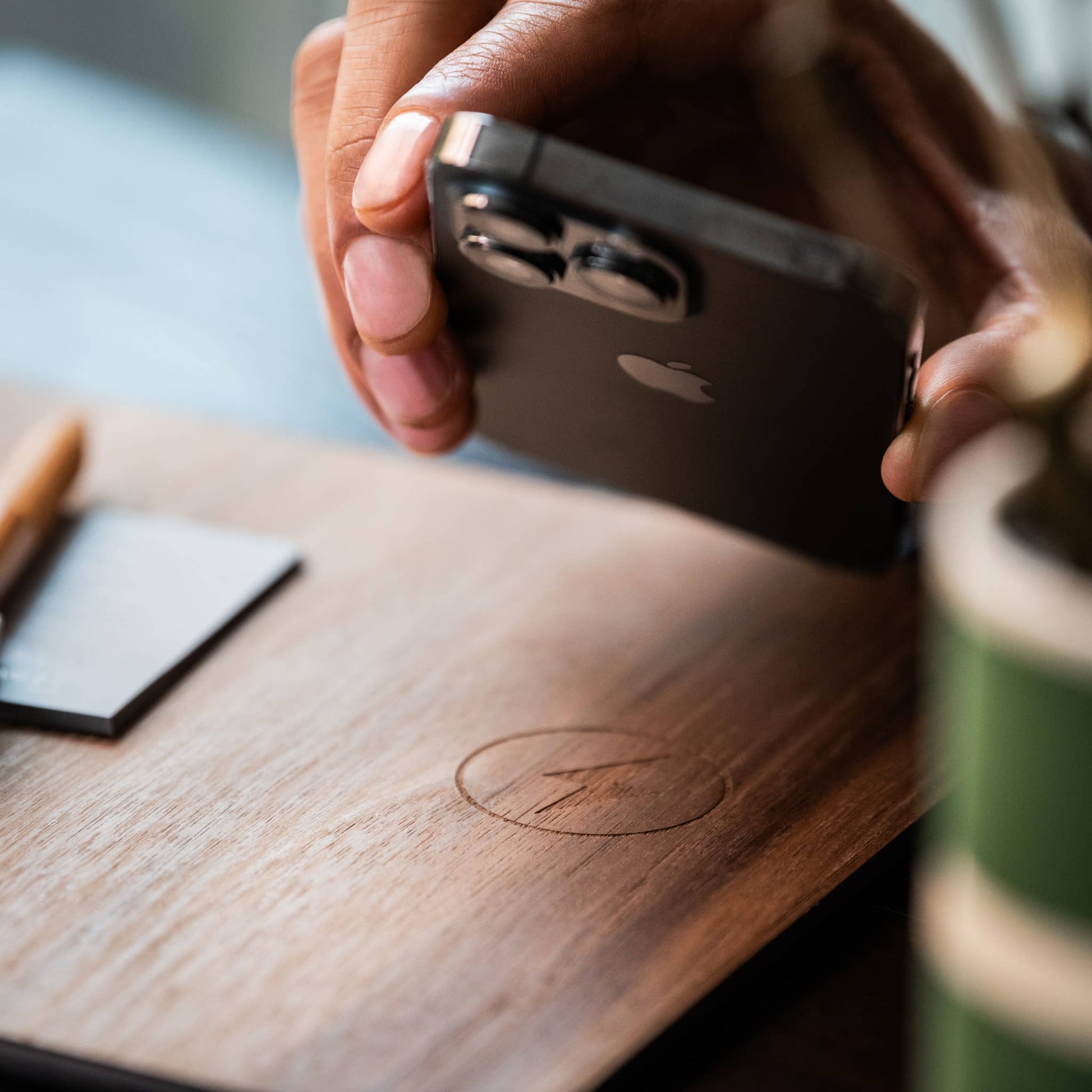 a hand about to place a iPhone onto a wooden mousepad with wireless charging