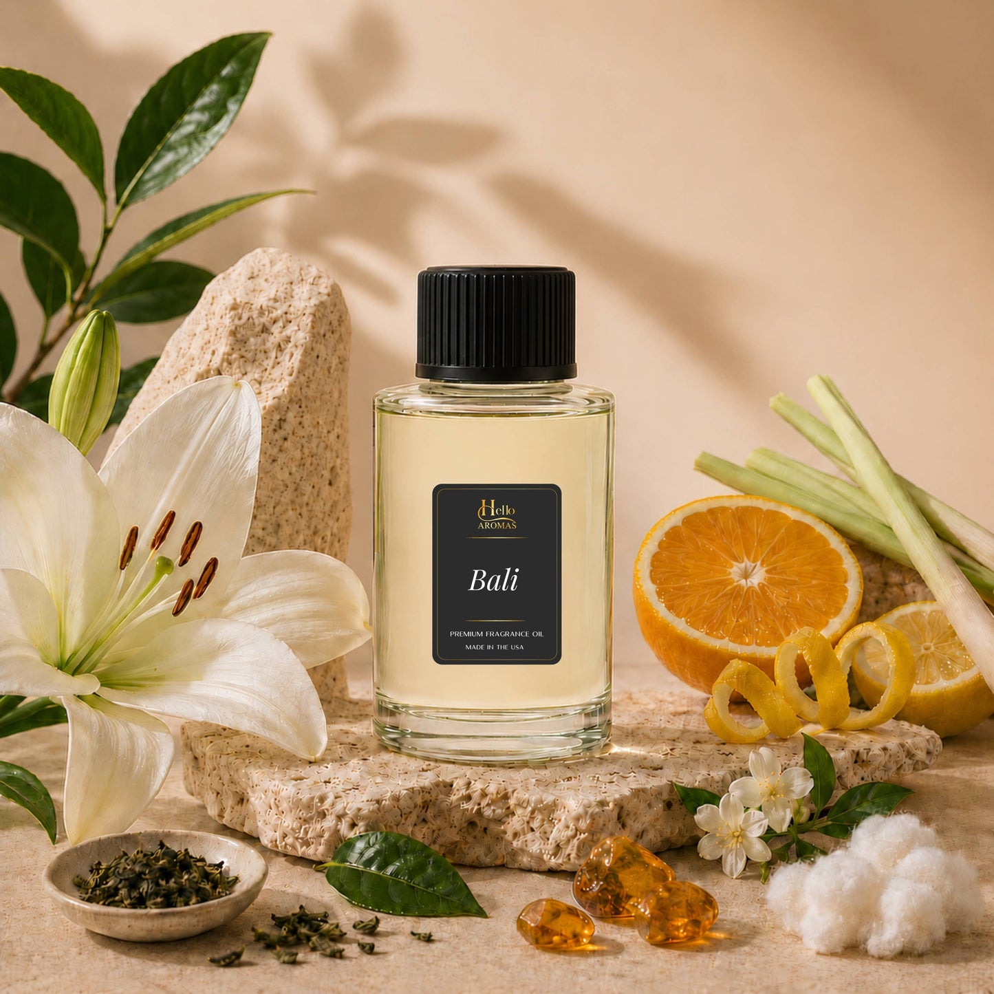 A clear glass bottle of Bali incense oil with a black cap and black label, styled on a stone slab with a white lily flower, orange slices, lemongrass, cotton, and green leaves against a warm beige background.