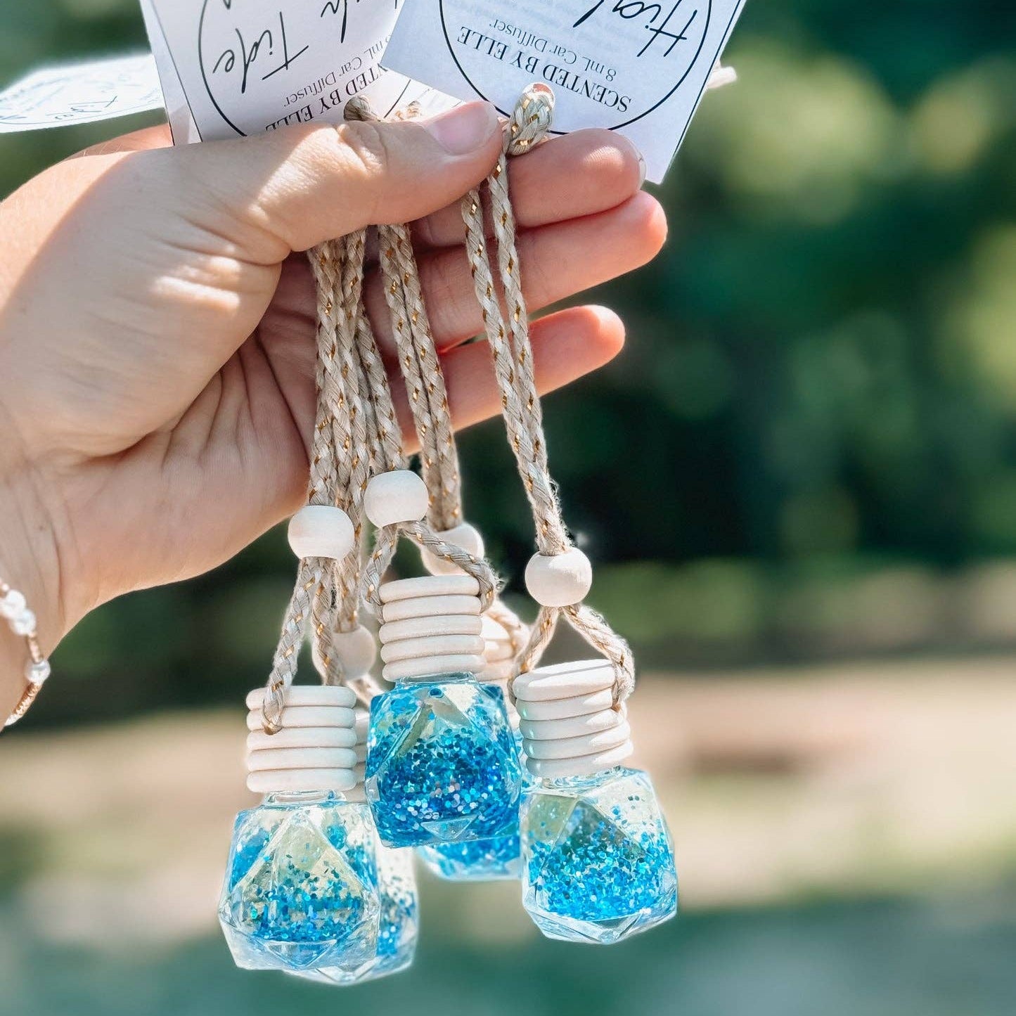 Hand holding three small glass jars with blue contents and decorative tags.