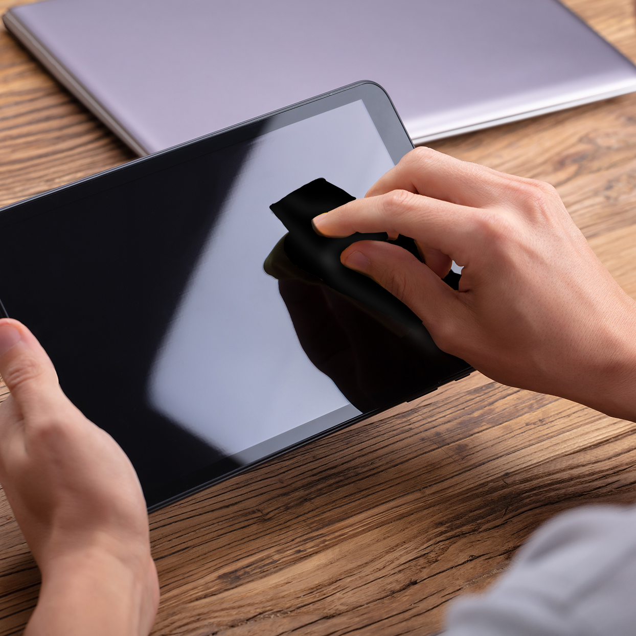 Person using a stylus on a tablet with a laptop in the background on a wooden table