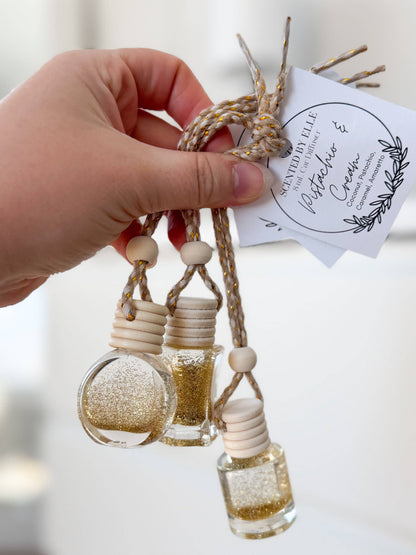 Hand holding a decorative hanging with small bottles and beads, featuring a brand label.