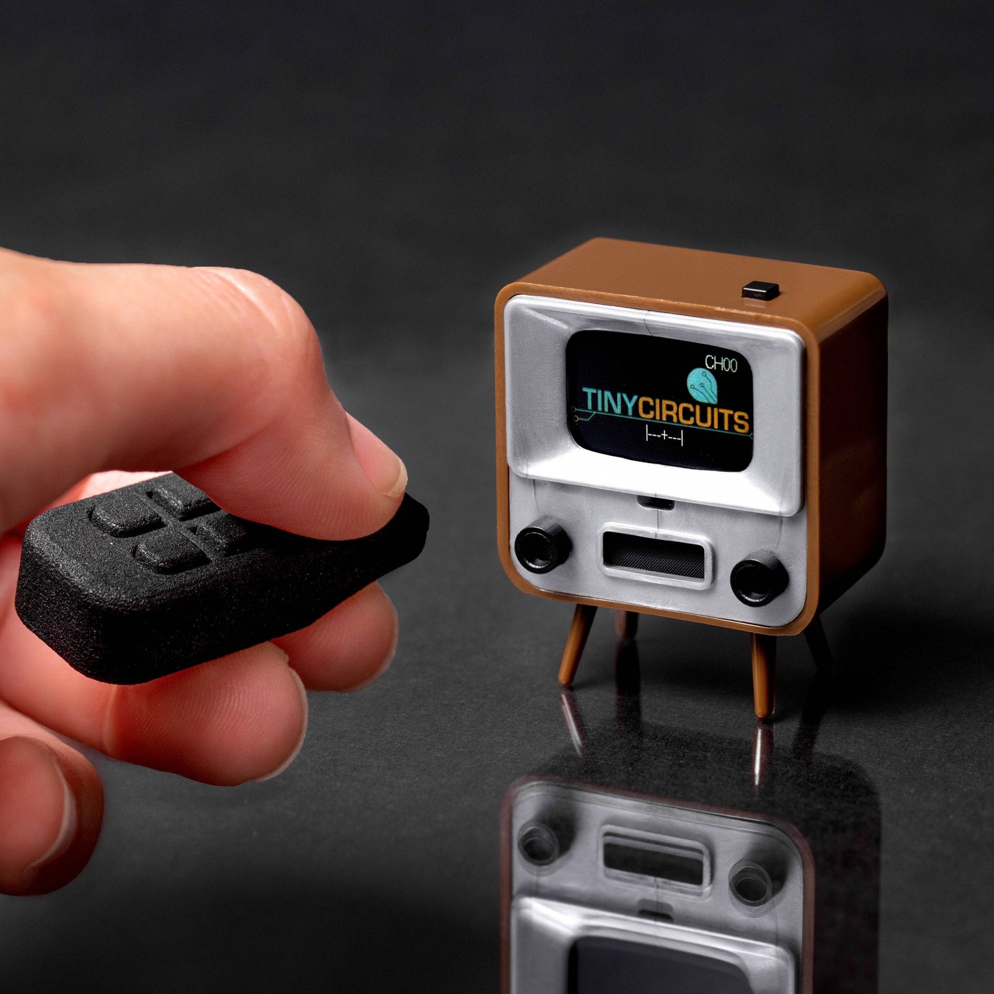 Small vintage-style radio with 'Tiny Circuits' branding held by a hand against a dark background