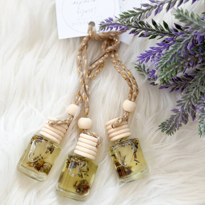 Three small glass bottles with wooden caps on a white surface with lavender flowers.