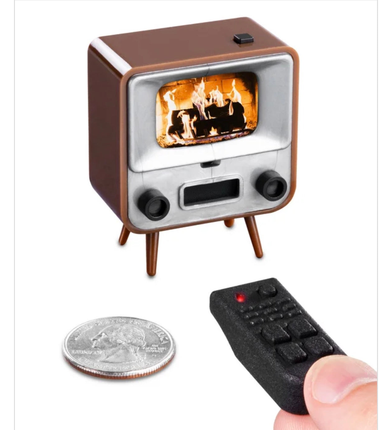 A miniature retro television set with a fireplace screen image on its display, shown alongside a coin for scale and a small black remote control held by a hand on a white background.