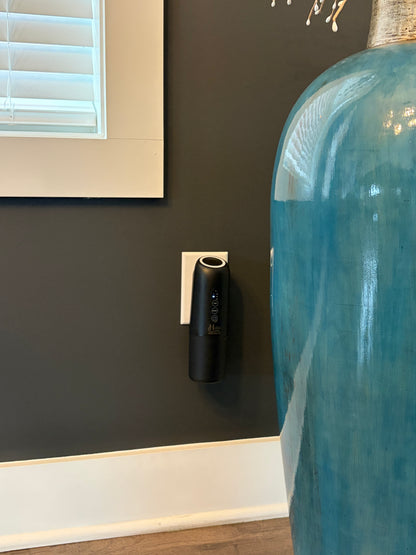 Black wall-mounted device on a dark wall next to a large blue vase.