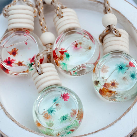 Set of three glass bottle keychains with floral designs on a white plate.