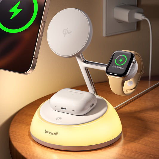 A Lamicall wireless charging stand on a wooden table, charging a smartphone, an Apple Watch Ultra, and white earbud cases. The stand has a glowing warm yellow base, a white charging platform, and a silver adjustable arm with a circular Qi2 logo.