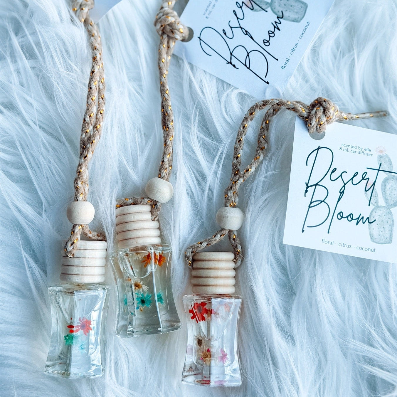 Three small glass bottles with wooden tops on a fluffy white surface, each labeled 'Desert Bloom'.
