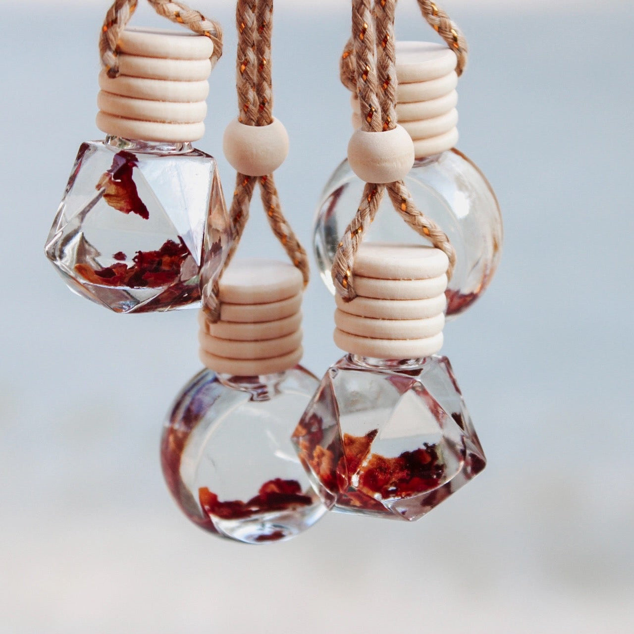Three hanging glass bottles with wooden stoppers on a light background