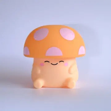 A cute, small mushroom-shaped character toy or figurine with a rounded peach body, a large orange cap with pink spots, and a smiling face, set against a soft light blue-gray gradient background.