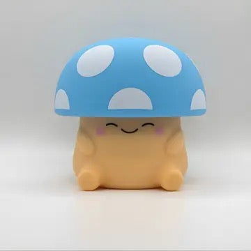 A cute, squishy toy figure with a smiling face under a large blue mushroom cap with white spots, set against a plain light gray background.