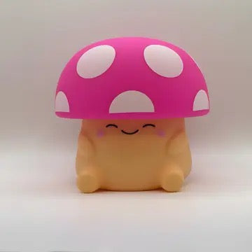 A cute mushroom-shaped squishy toy with a pink cap featuring white spots and a smiling beige body, set against a plain light gray background.