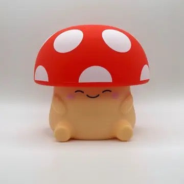 A cute, small mushroom-shaped figure with a red cap, white spots, and a smiling face on a light gray background.