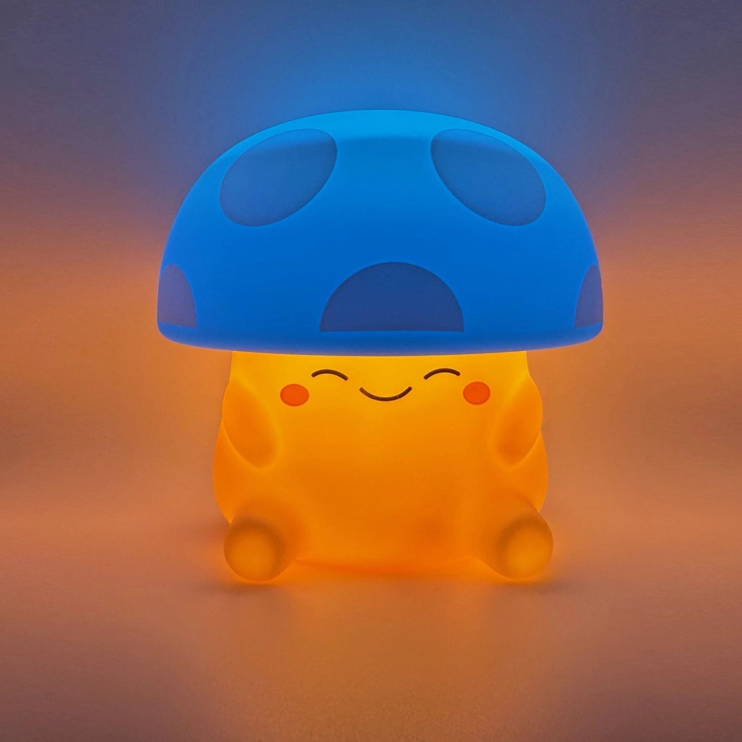 A cute mushroom-shaped glowing night light with a blue cap and a warm orange body, sitting on a soft gradient surface.