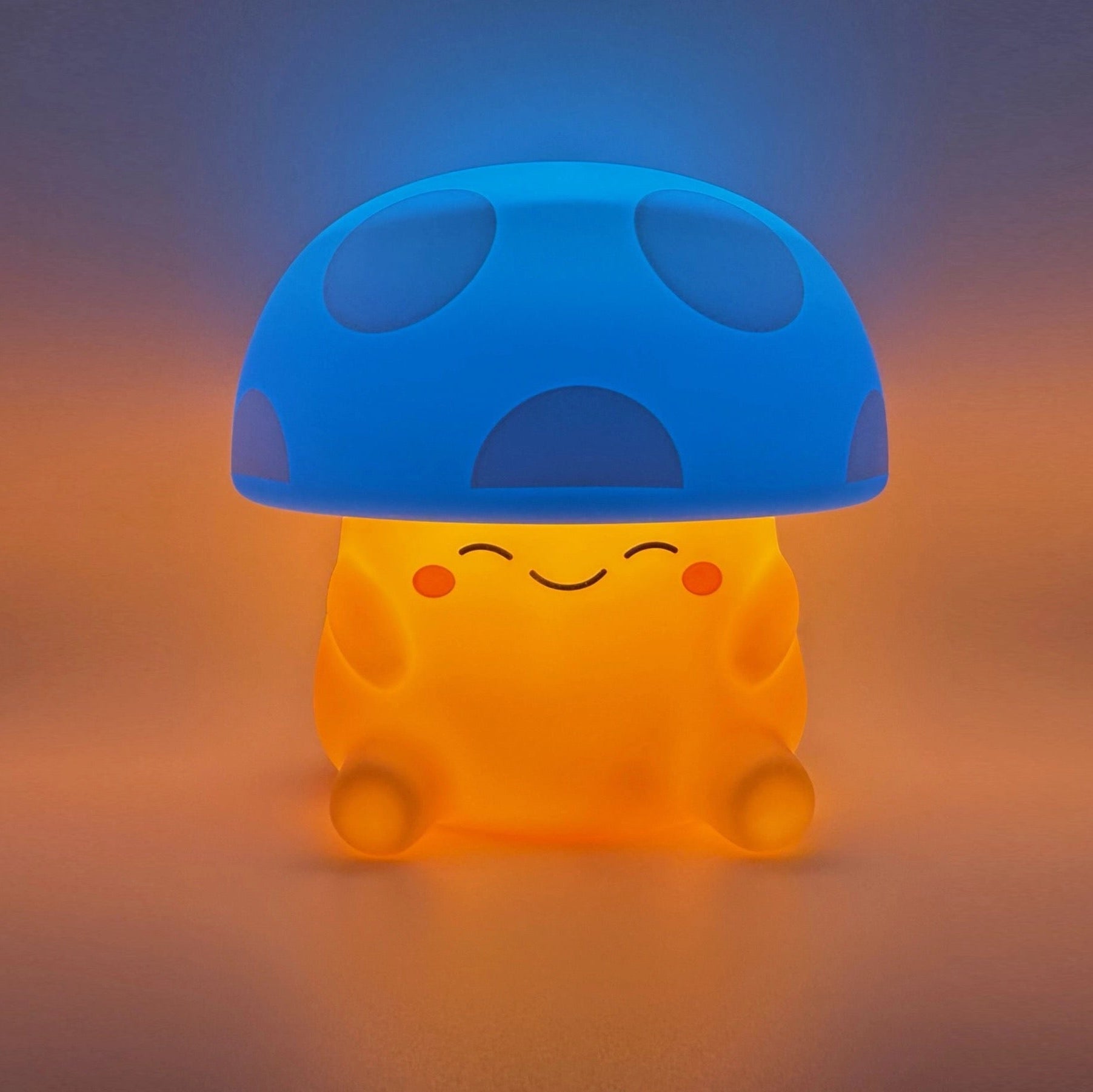 A cute mushroom-shaped glowing night light with a blue cap and a warm orange body, sitting on a soft gradient surface.