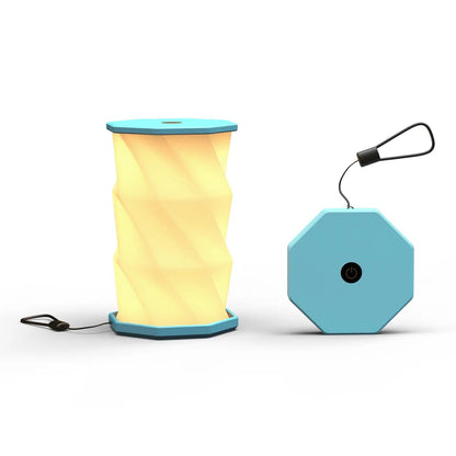 A portable folding lamp  shown on a clean white background. The lamp is unfolded and illuminated with a geometric, faceted design in warm yellow.