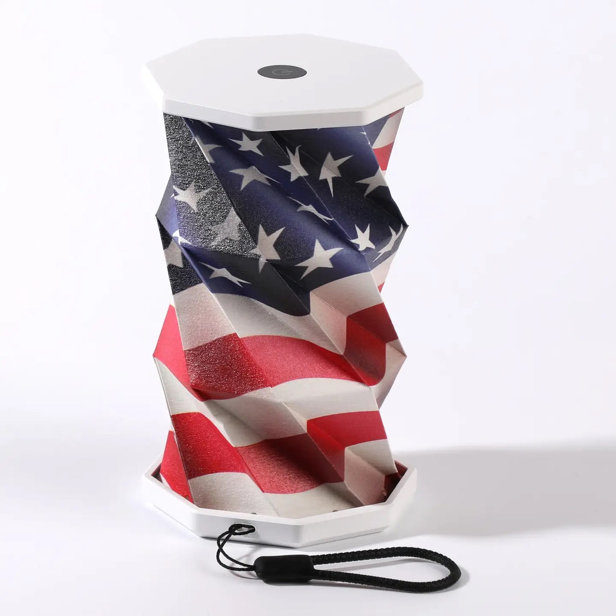 A USA Flag portable folding lamp  shown on a clean white background. The lamp is unfolded and illuminated with a geometric, faceted design in warm yellow.