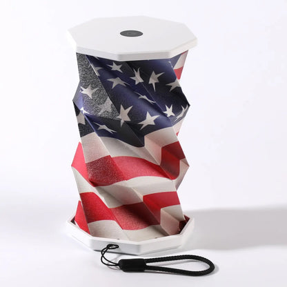 A USA Flag portable folding lamp  shown on a clean white background. The lamp is unfolded and illuminated with a geometric, faceted design in warm yellow.
