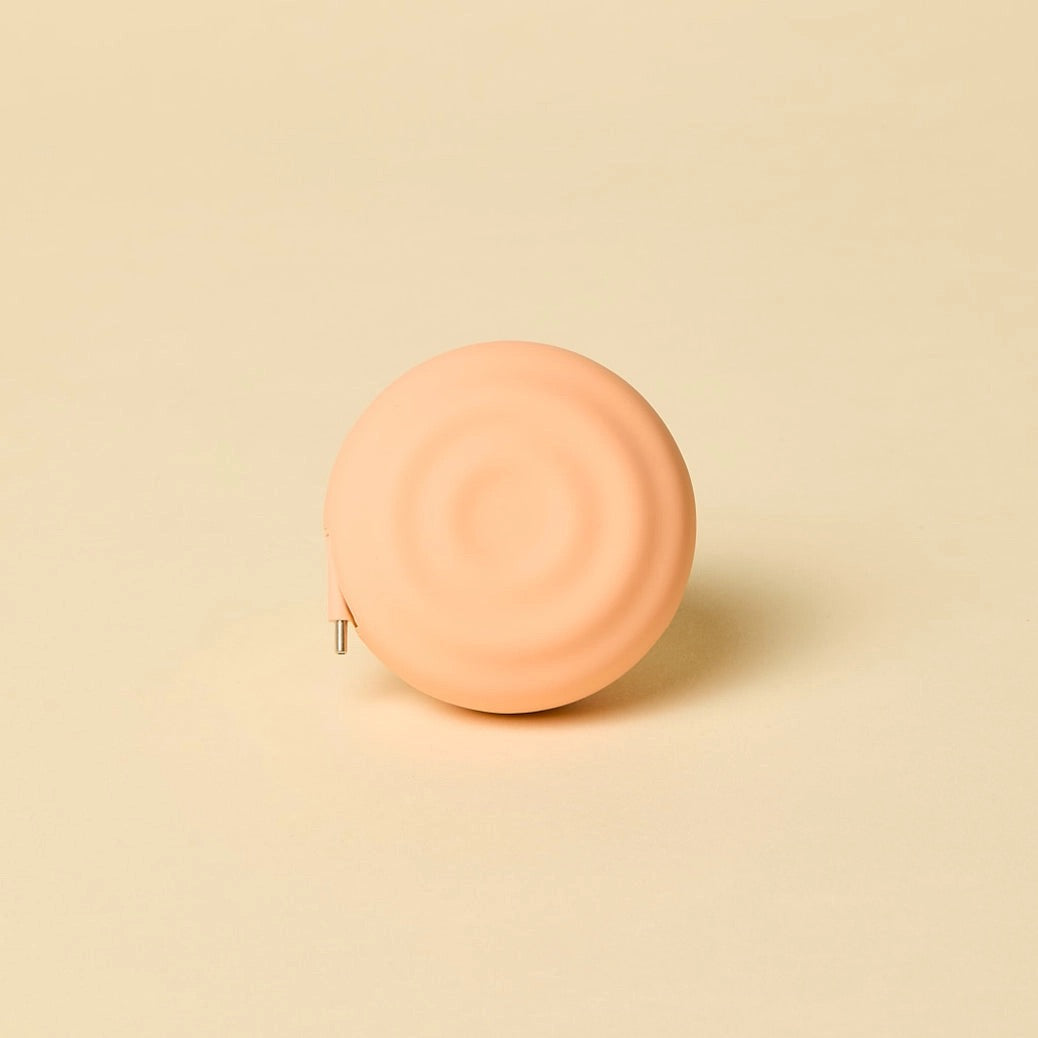 Round peach-colored retractable charger on a beige background
