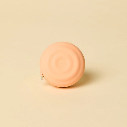 Round peach-colored retractable charger on a beige background