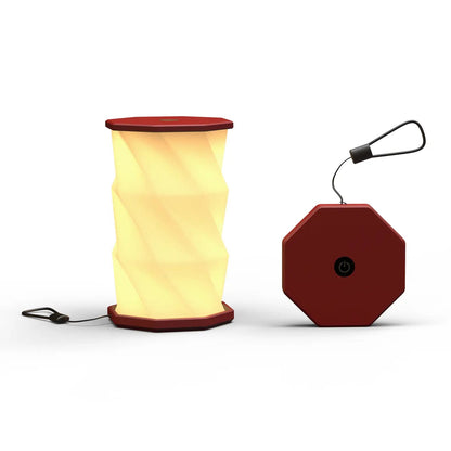 A portable folding lamp  shown on a clean white background. The lamp is unfolded and illuminated with a geometric, faceted design in warm yellow.