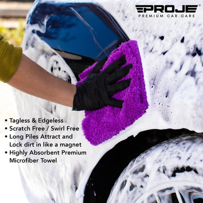 A person wearing a black glove washes a white foamy car with a bright purple microfiber towel. The Proje Premium Car Care logo is visible in the top right, and product feature text is shown on the left.