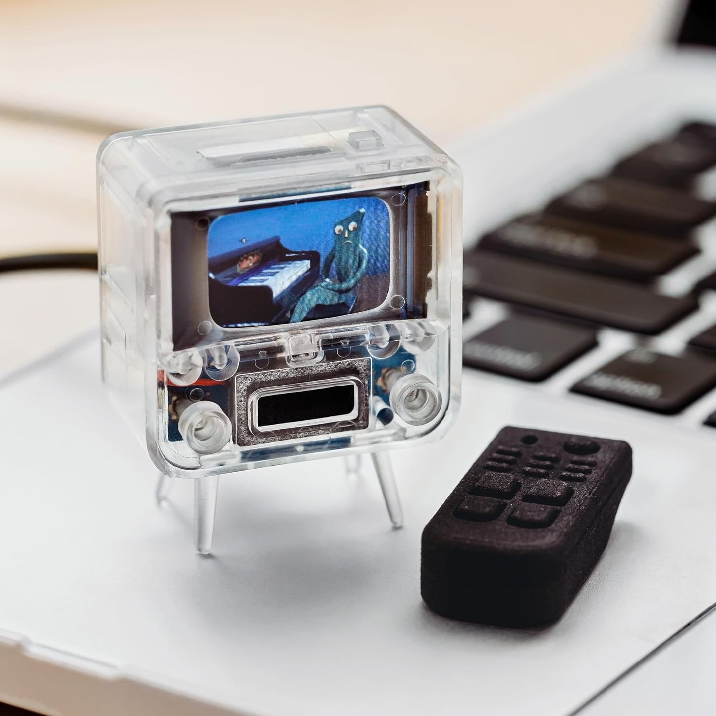 Small transparent electronic device with a screen on a desk next to a keyboard