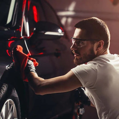 Man polishing a car with a red towel in a garage setting