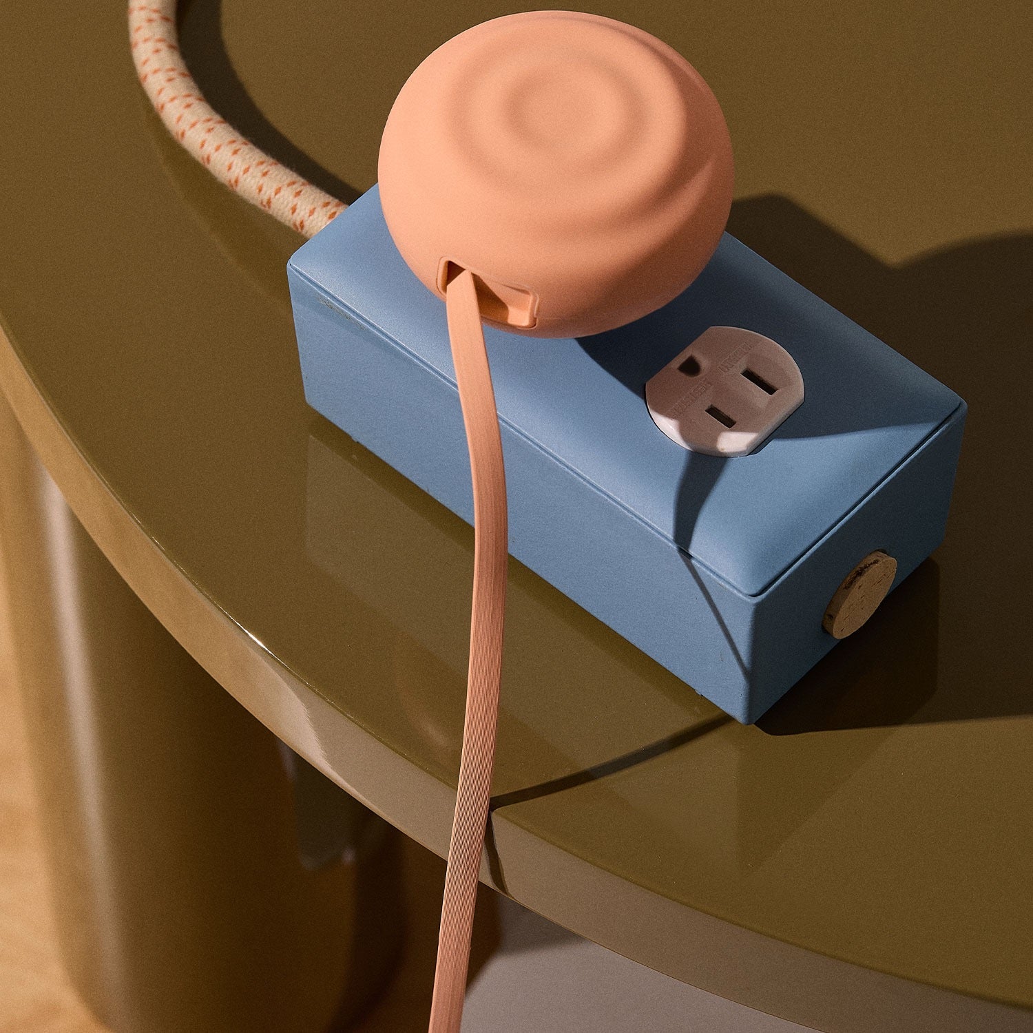 Blue power strip with peach-colored retractable charger on a reflective surface