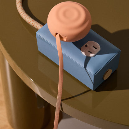 Blue power strip with peach-colored retractable charger on a reflective surface