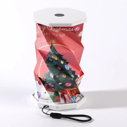 A Christmas portable folding lamp  shown on a clean white background. The lamp is unfolded and illuminated with a geometric, faceted design in warm yellow.