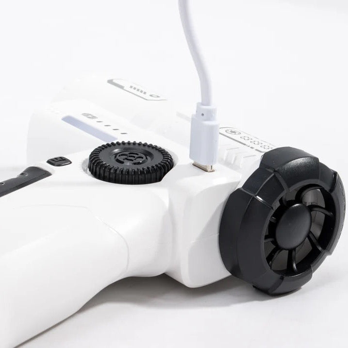 A close-up of a white handheld electronic device with black circular dials and a white charging cable plugged into it, photographed on a clean white background.