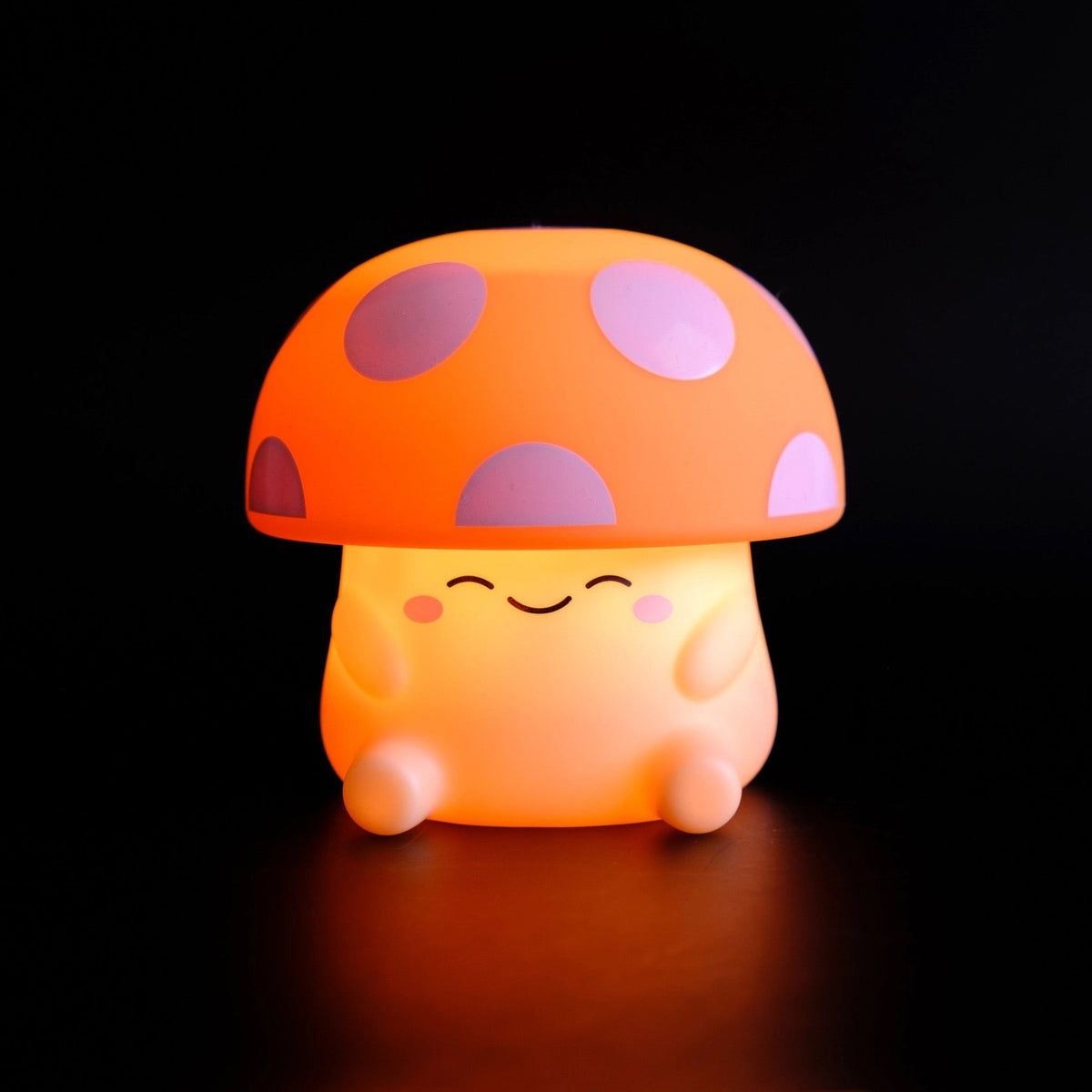 A cute mushroom-shaped night light glowing warmly against a solid black background. The toy features a rounded body and a domed cap with purple spots on an orange base, complete with a smiling face.