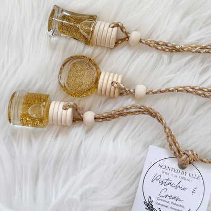 Two decorative necklaces with small glass bottles filled with gold glitter on a white textured surface, accompanied by a card.