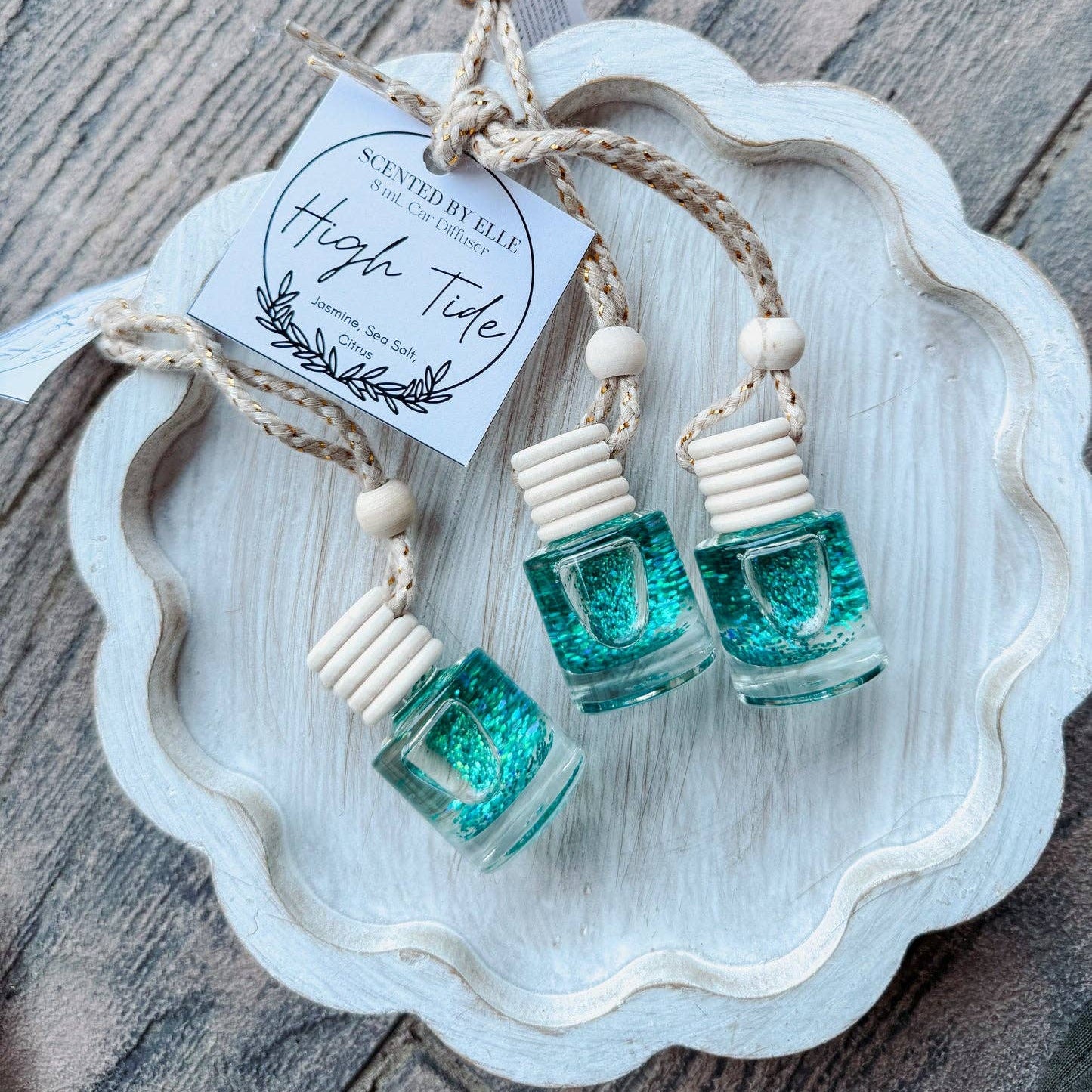 Three small green glittery bottles hanging on a string with a decorative tag on a wooden surface.