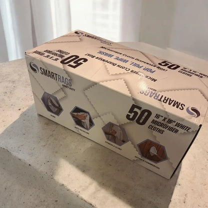 A beige cardboard box of smartrags heavy-duty 16x16 inch white microfiber cloths, labeled as a ’pop pull dispenser box’ containing 50 pieces.