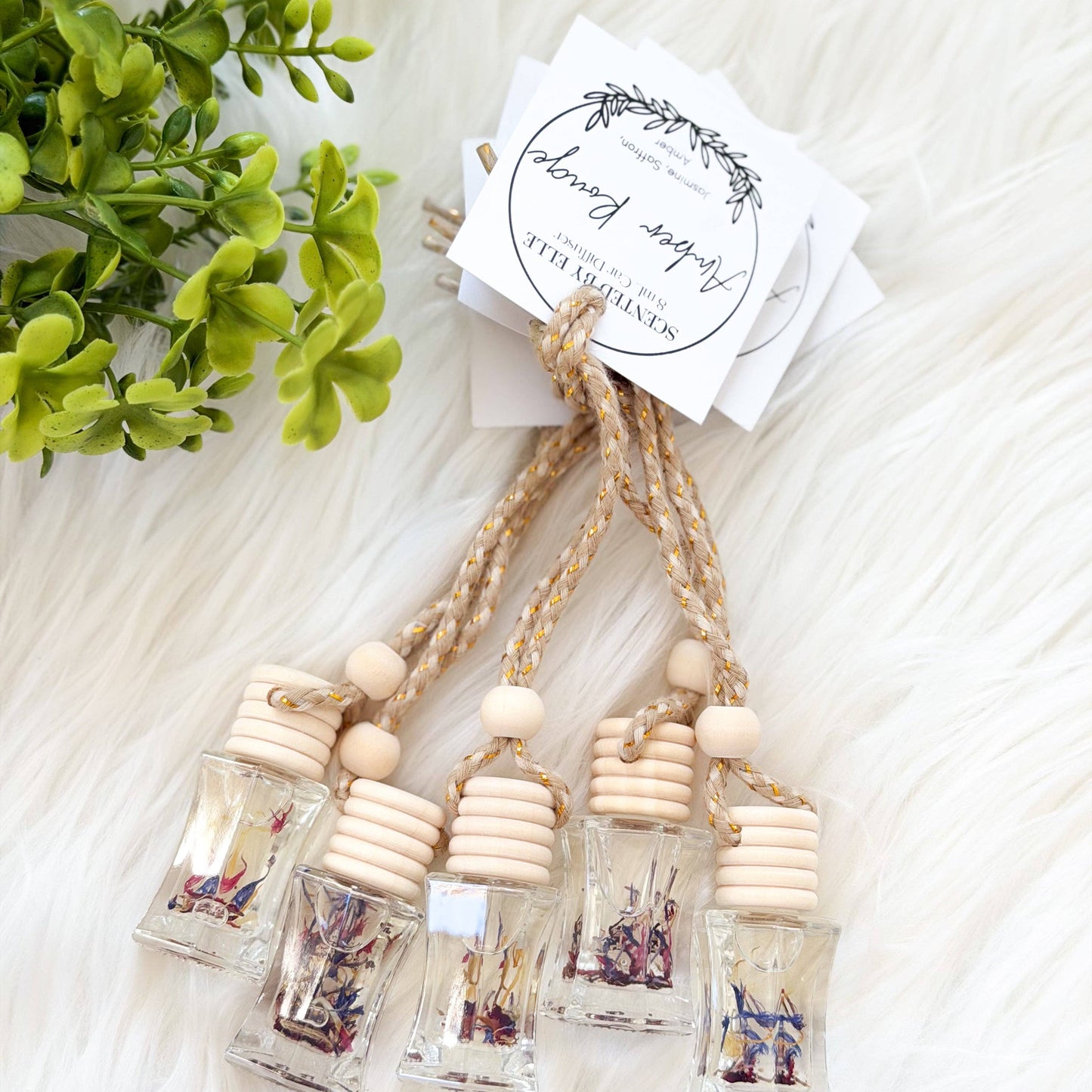 Decorative hanging bottles with wooden beads on a white surface with greenery.
