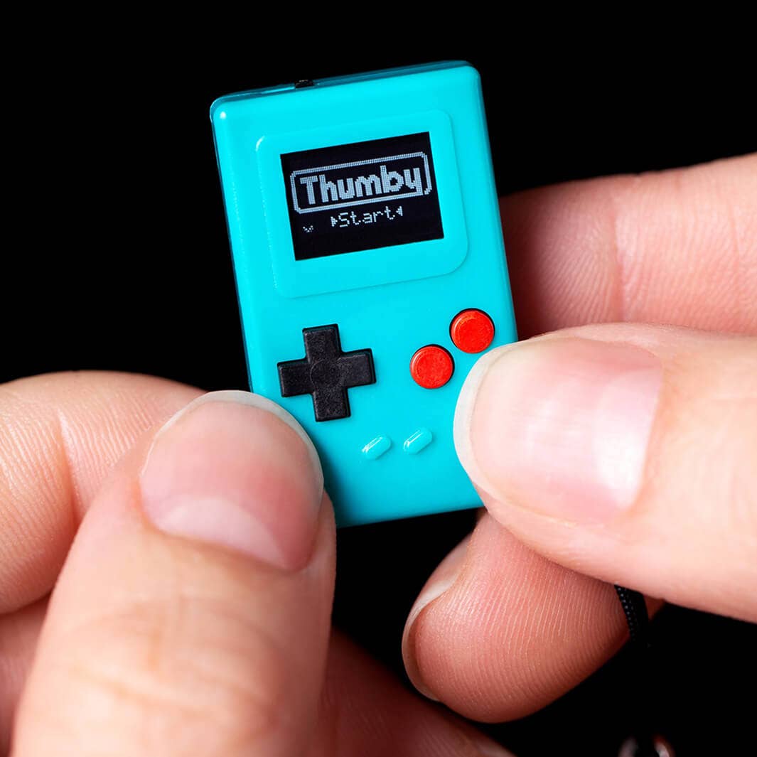 Small teal game with 'Thumby' branding held between fingers against a black background